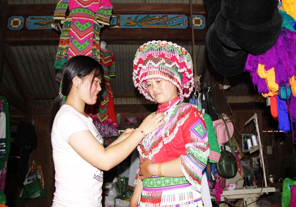 Giàng Thị Tùng  (bên trái) giúp khách mặc thử trang phục Hmông  tại tiệm may của mẹ. 