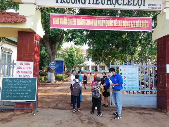 Đoàn viên thanh niên huyện Cư M'gar túc trực ngay tại cổng trường, hướng dẫn các em học sinh  Trường Tiểu học Lê Lợi (thị trấn Quảng Phú) rửa tay sát khuẩn.  Ảnh: Đỗ Lan