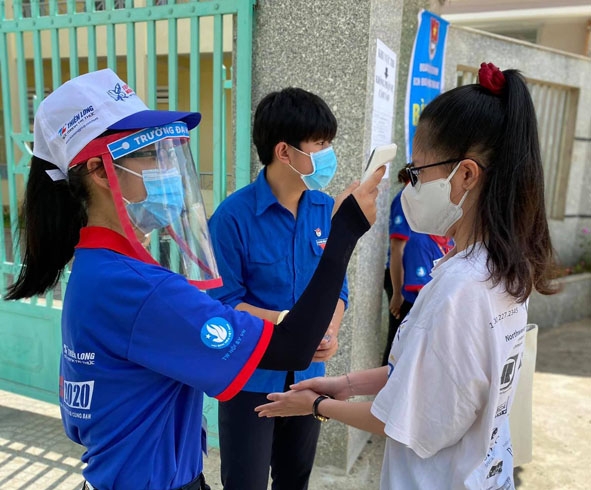 Thanh niên tình nguyện hỗ trợ thí sinh đo thân nhiệt và rửa tay sát khuẩn trước khi vào phòng thi.