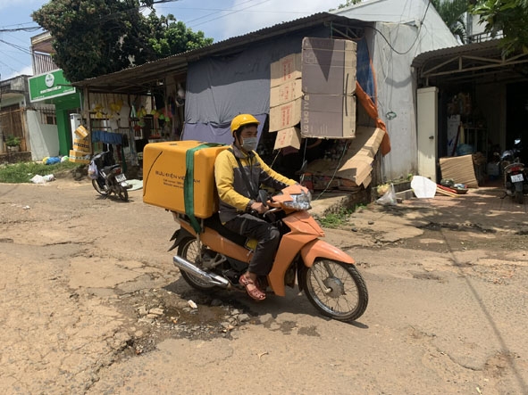 Bưu tá Lê Văn Gia Hải (Bưu điện tỉnh Đắk Lắk) chạy xe giao hàng qua đoạn đường nham nhở ổ gà giữa trưa.