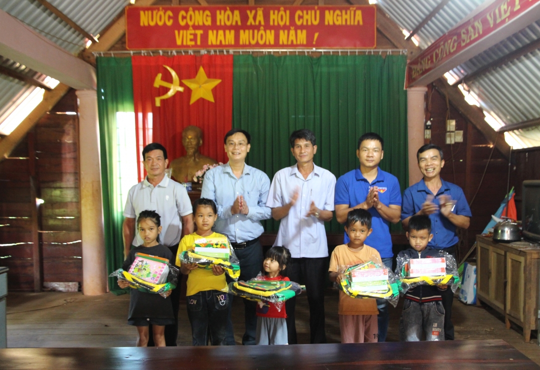 Đại diện Báo Đắk Lắk và buôn Cuôr Kăp trao quà tặng các em học sinh.