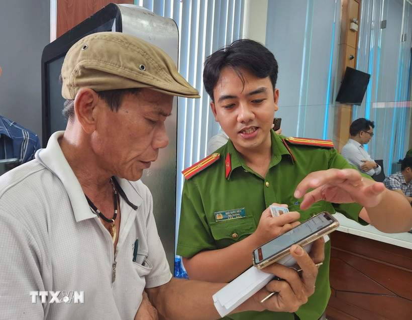 Cán bộ công an hướng dẫn người dân thao tác xin cấp phiếu lý lịch tư pháp trên ứng dụng VNeID. Ảnh: TTXVN