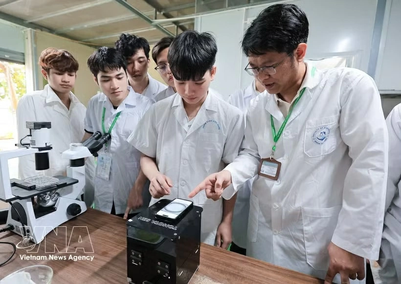 A lecturer of the Vietnam National University of Agriculture instructs students in how to use a piece of equipment integrated with AI and IoT to conduct research. (Photo: VNA)