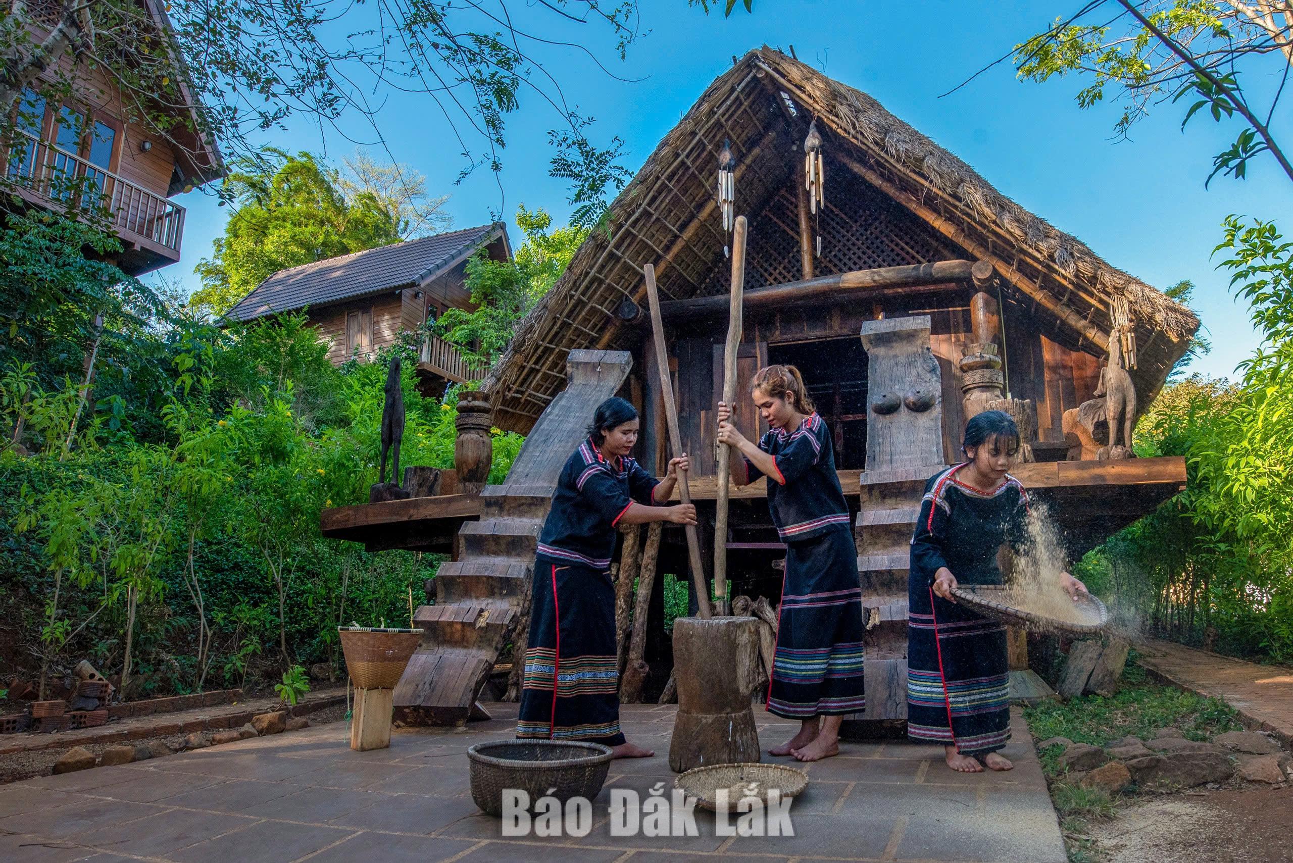 Ede women pounding rice in front of a traditional longhouse.