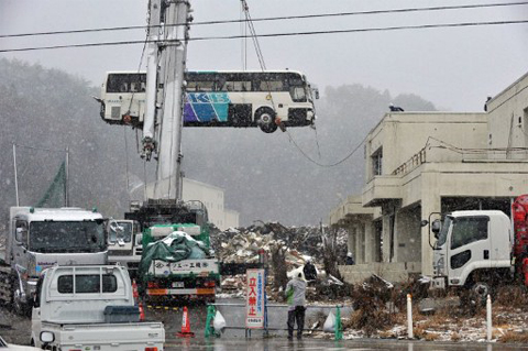 Một chiếc xe buýt được cẩu ra khỏi một nóc nhà ở quận Ogatsu, thành phố Ishinomaki, tỉnh Miyagi, hôm 10-3