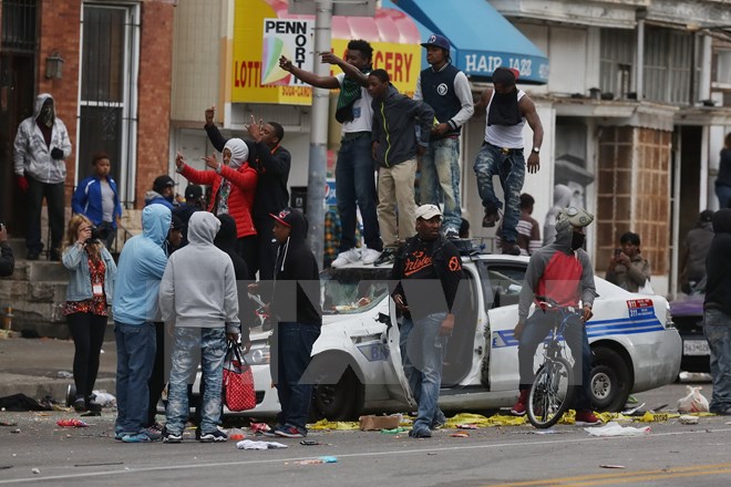 Những người biểu tình bạo động phá hủy xe cảnh sát ở Baltimore. (Nguồn: AFP/TTXVN)