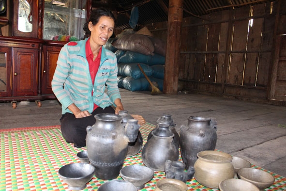 Bà H’Lưm Uông bên các sản phẩm gốm độc đáo do chính tay mình làm ra.