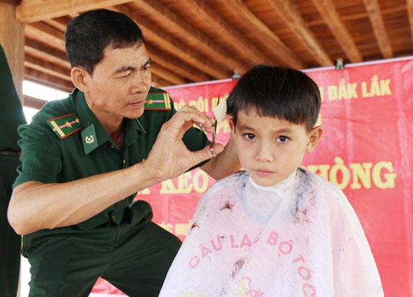 Thiếu tá Vũ Văn Tín tỉ mẩn cắt tóc cho học sinh.  