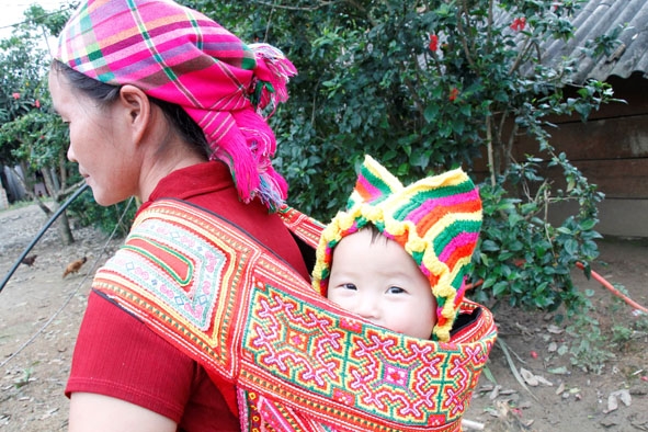 Em bé người Mông đi chơi cùng mẹ trên chiếc địu với họa tiết thêu tay truyền thống.
