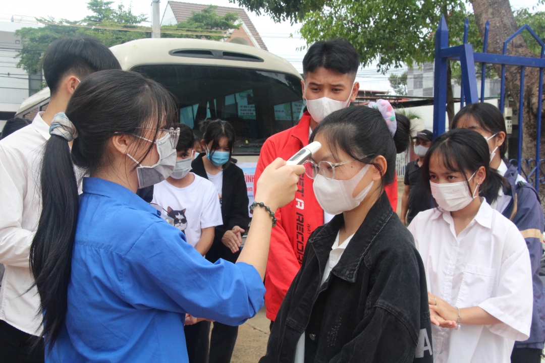 Tình nguyện viên hỗ trợ đo thân nhiệt cho các thí sinh tại điểm thi Trường THPT Lê Duẩn (TP. Buôn Ma Thuột).